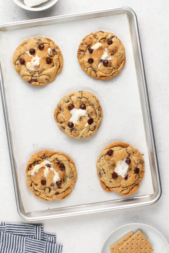Five baked giant s'mores cookies on a parchment-lined baking sheet.