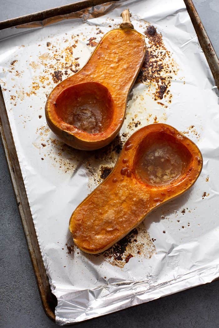 Roasted butternut squash halves on a foil-lined sheet tray