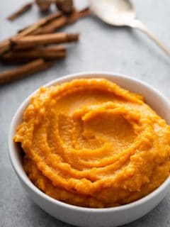 Butternut squash puree in a white bowl with whole spices and a spoon in the background