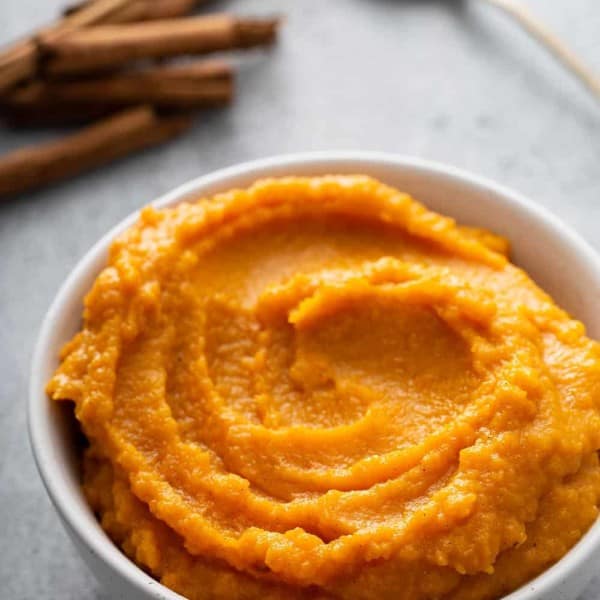 Butternut squash puree in a white bowl with whole spices and a spoon in the background