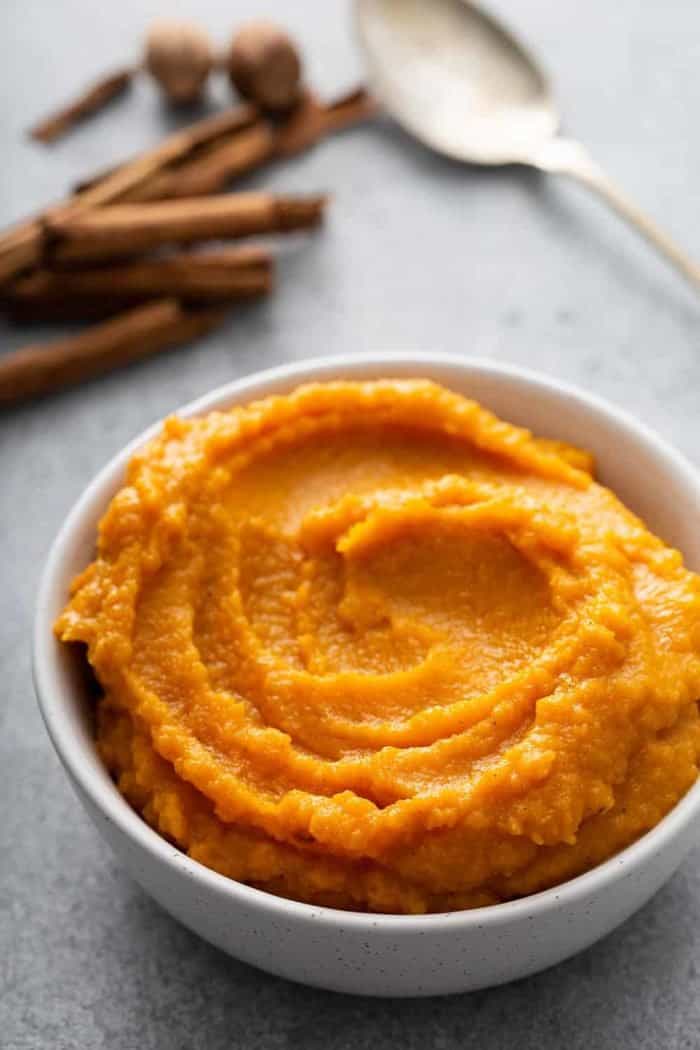 Butternut squash puree in a white bowl with whole spices and a spoon in the background