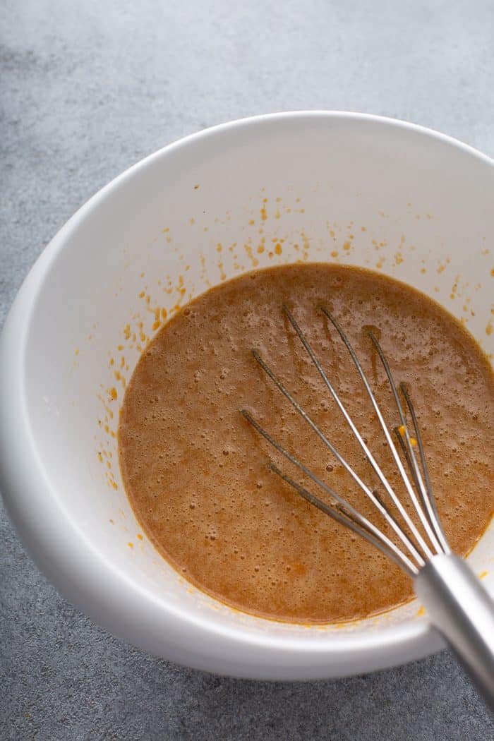 Wet ingredients for butternut squash bread being whisked together in a white mixing bowl