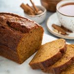 Sliced loaf of butternut squash bread on a cutting board with a cup f chai and spices in the background