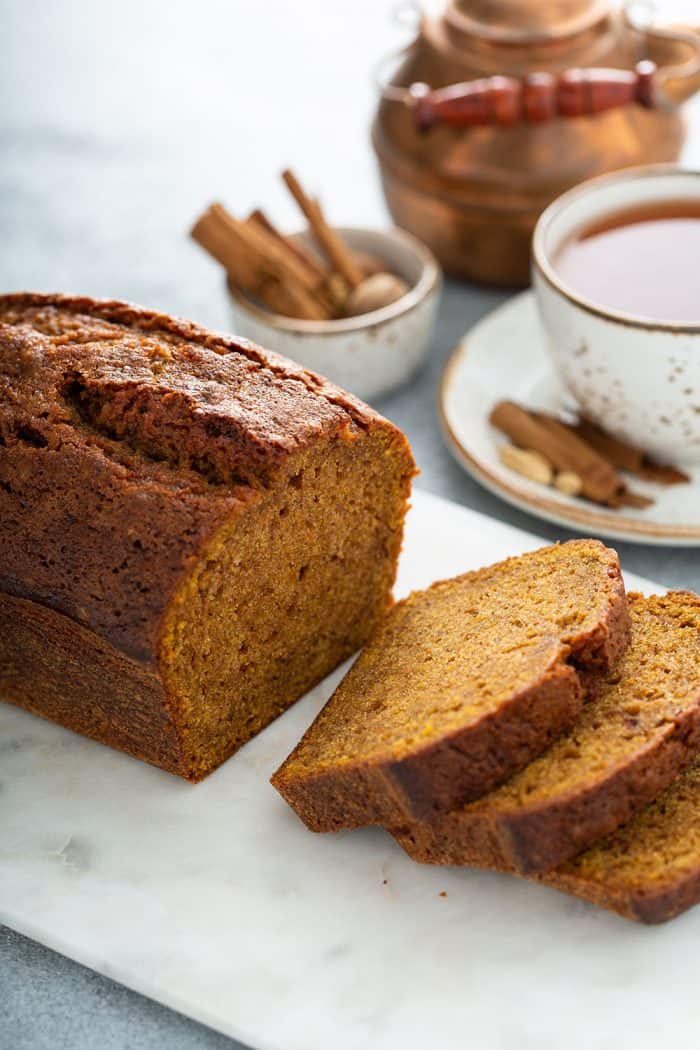 Sliced loaf of butternut squash bread on a cutting board with a cup f chai and spices in the background