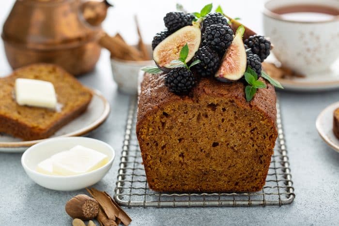 Loaf of butternut squash bread topped with figs and berries on a metal cooling rack