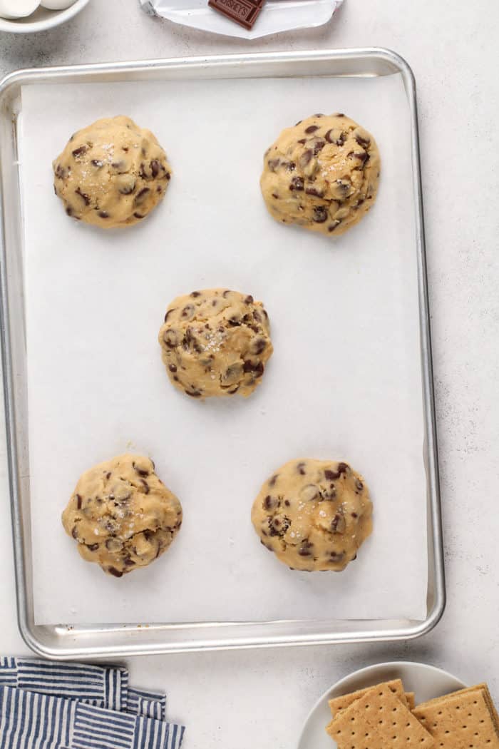 Five assembled giant s'mores cookies on a parchment-lined baking sheet, ready to go in the oven.