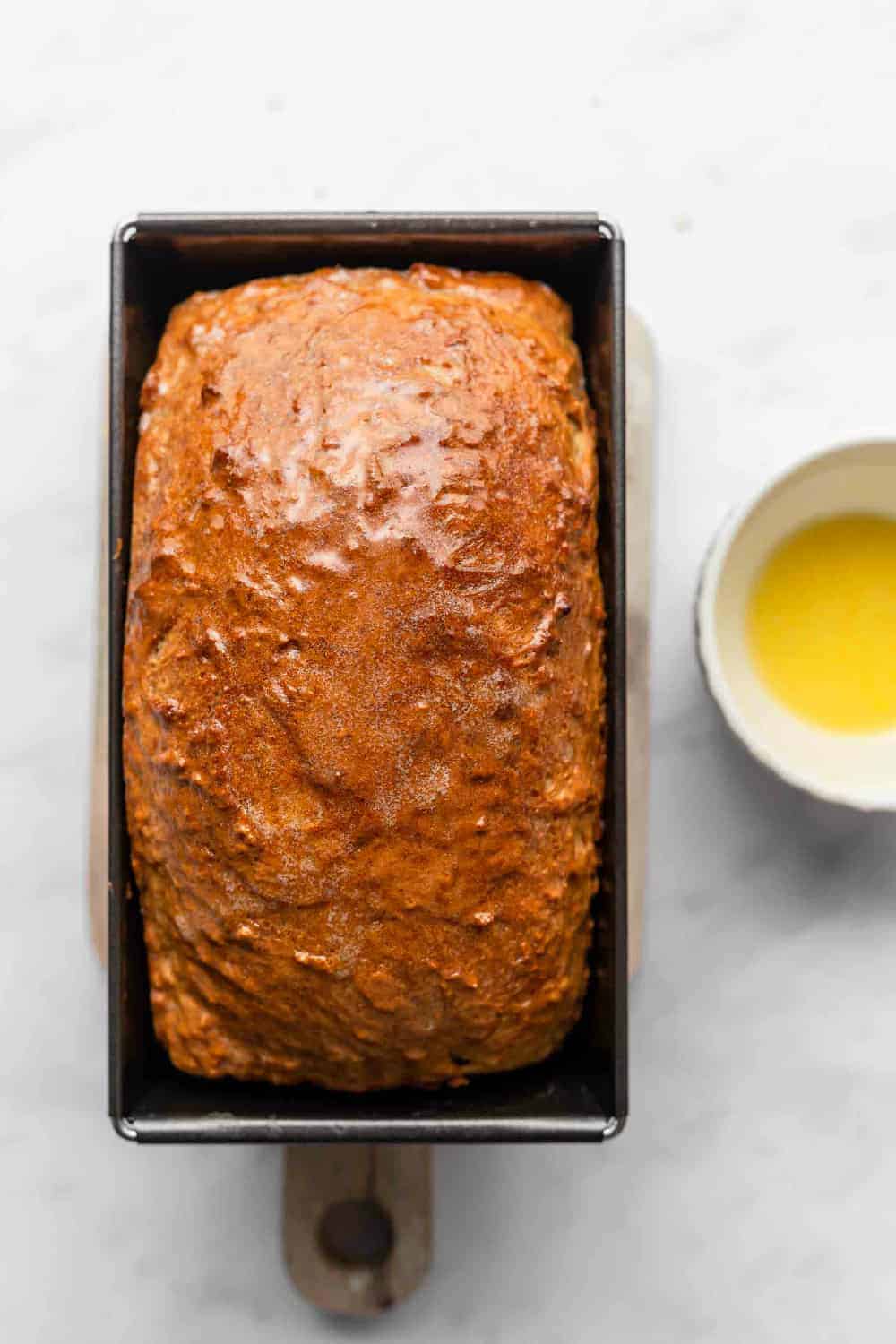Freshly baked loaf of beer bread in a loaf pan next to a bowl of melted butter
