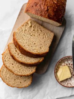 Loaf of beer bread sliced on a wooden cutting board, next to a plate of butter