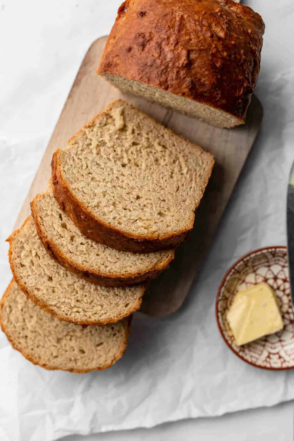 Loaf of beer bread sliced on a wooden cutting board, next to a plate of butter