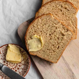 Buttered beer bread on a wooden board next to a plate of butter