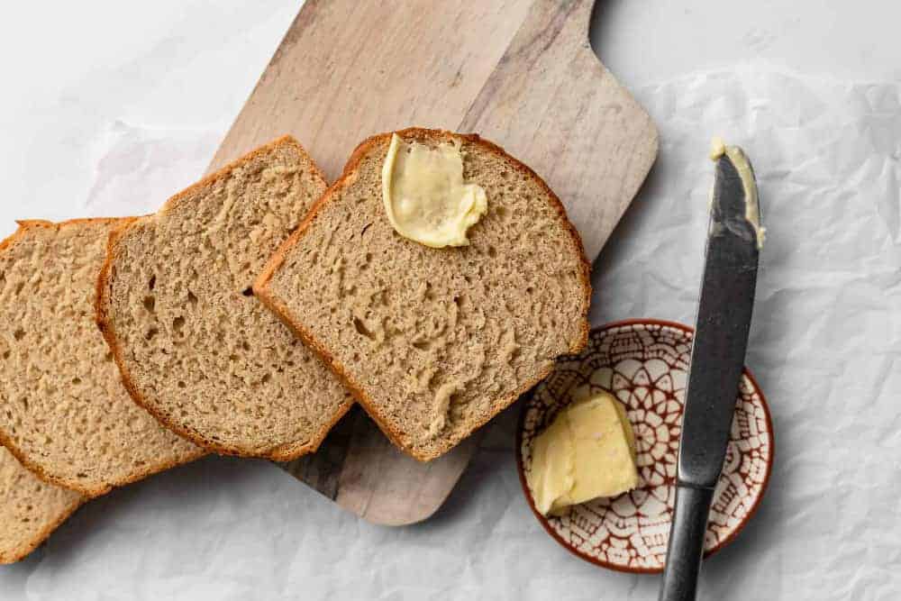 Slices of beer bread on a wooden board next to a plate of butter