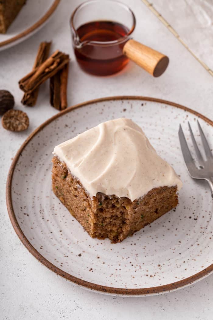 Slice of zucchini cake topped with maple cream cheese frosting with a bite taken from the corner.