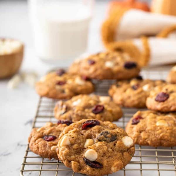 Pumpkin oatmeal cookies scattered on a wire cooling rack with a glass of milk in the background