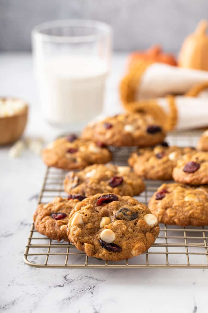 Pumpkin oatmeal cookies scattered on a wire cooling rack with a glass of milk in the background