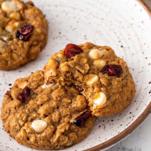 Three pumpkin oatmeal cookies on a cream-colored plate. One cookie has a bite taken out of it