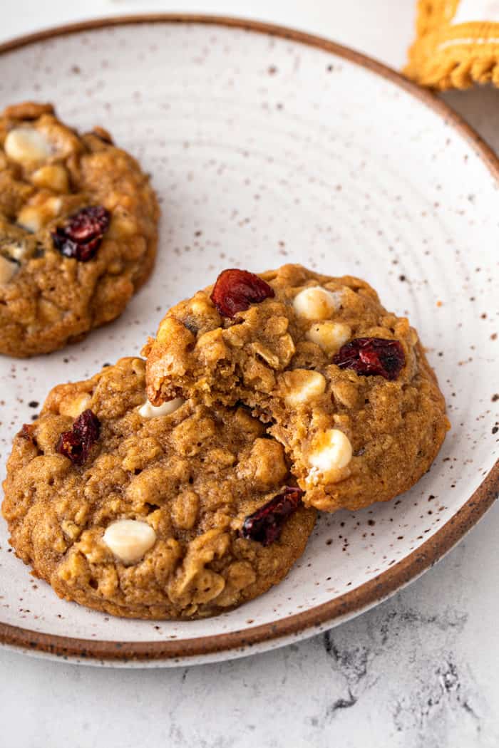 Three pumpkin oatmeal cookies on a cream-colored plate. One cookie has a bite taken out of it