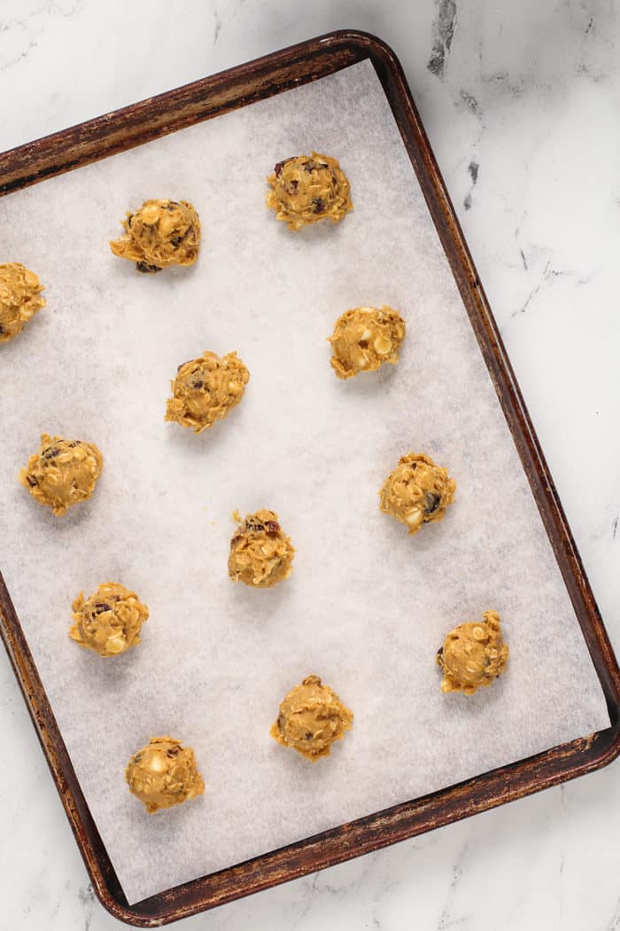 Pumpkin oatmeal cookie dough portioned onto a parchment-lined baking sheet, ready to bake