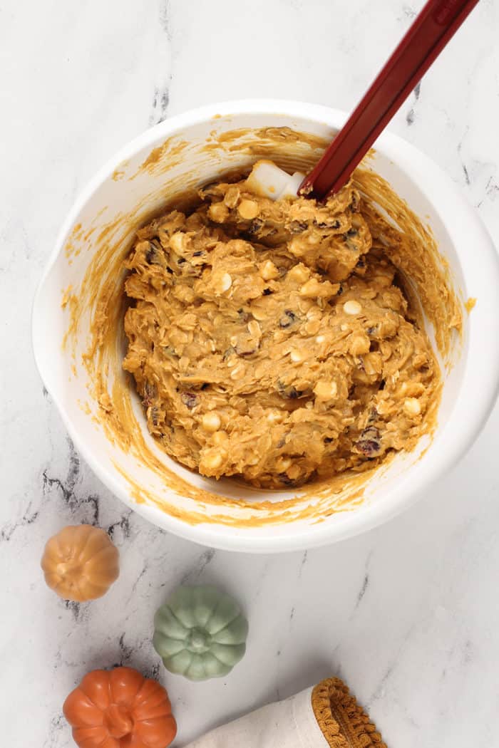 Spatula stirring together pumpkin oatmeal cookie dough in a white mixing bowl