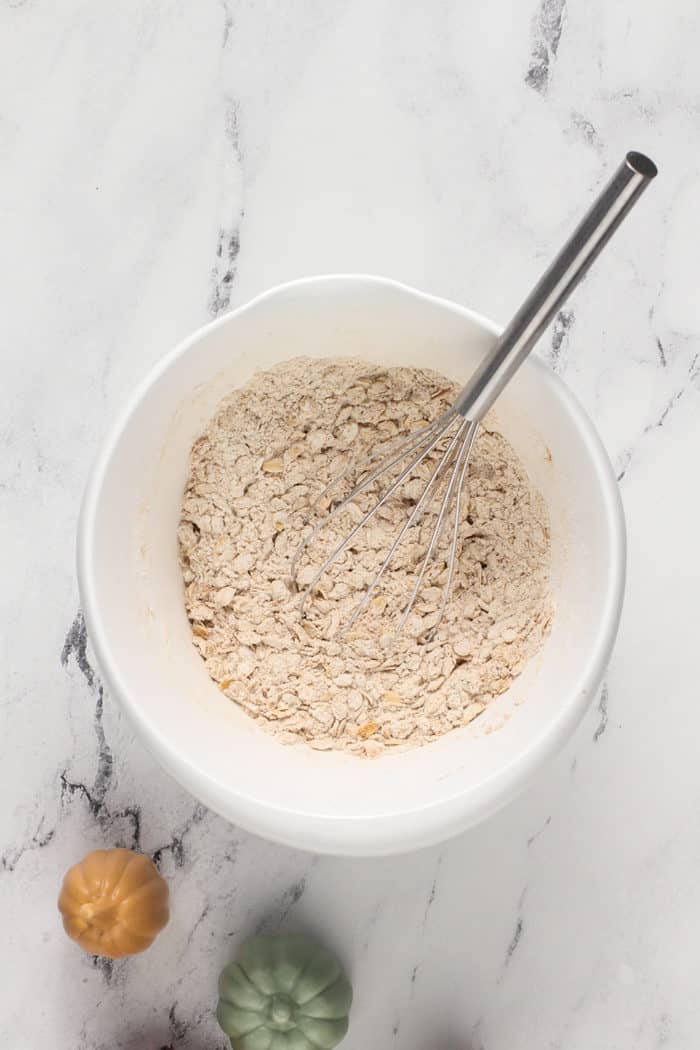 Dry ingredients for pumpkin oatmeal cookies being whisked together in a white bowl on a marble countertop