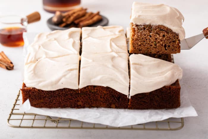 Slice being lifted up from a zucchini cake topped with maple cream cheese frosting.