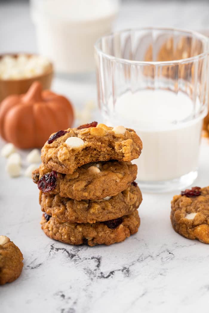 Four pumpkin oatmeal cookies stacked next to a glass of milk
