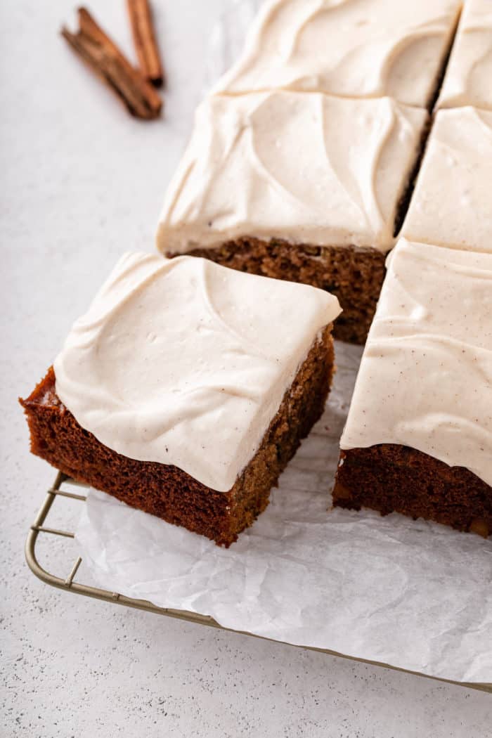 Corner slice pulled away from a zucchini cake topped with maple cream cheese frosting.