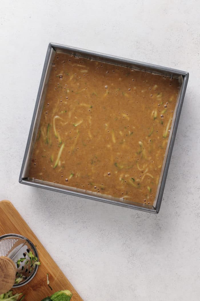 Zucchini cake batter in a greased cake pan, ready to go in the oven.