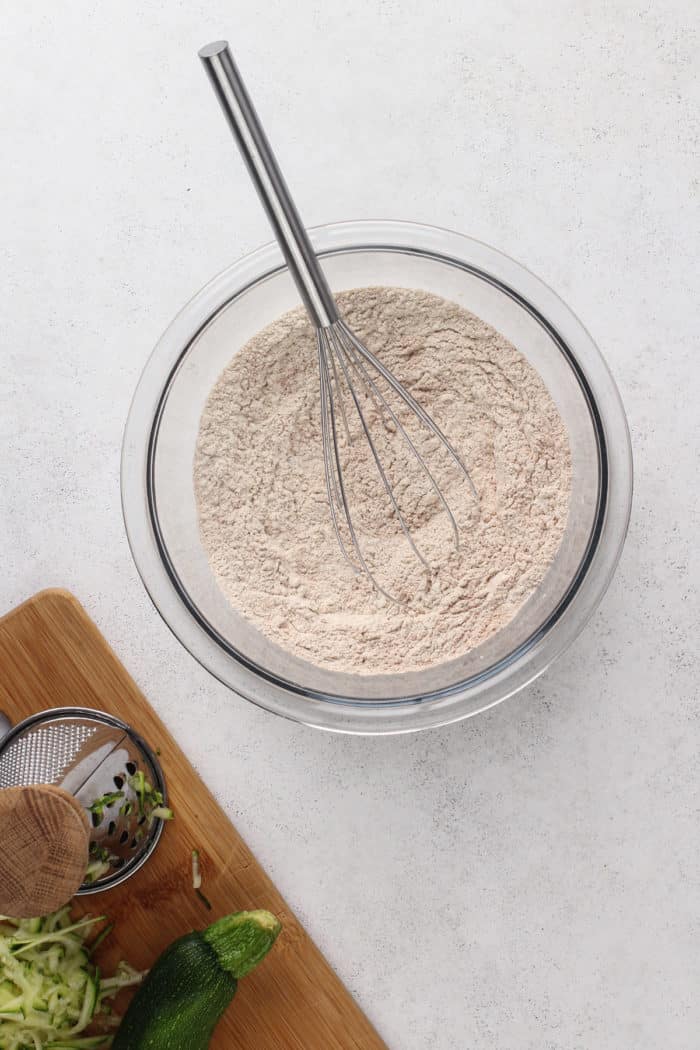 Dry ingredients for zucchini cake whisked together in a glass mixing bowl.