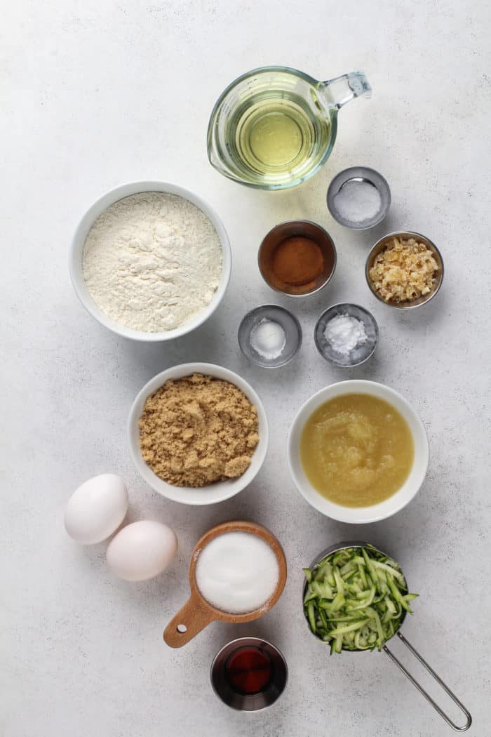 Ingredients for zucchini cake arranged on a light gray countertop.