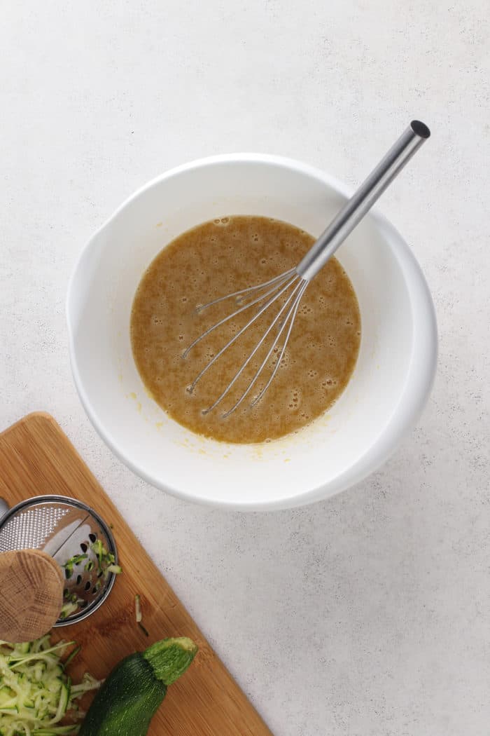 Wet ingredients for a zucchini cake whisked together in a white mixing bowl.