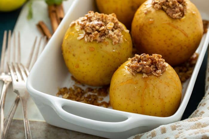 Close up of baked apples in a white baking dish, drizzled with caramel sauce