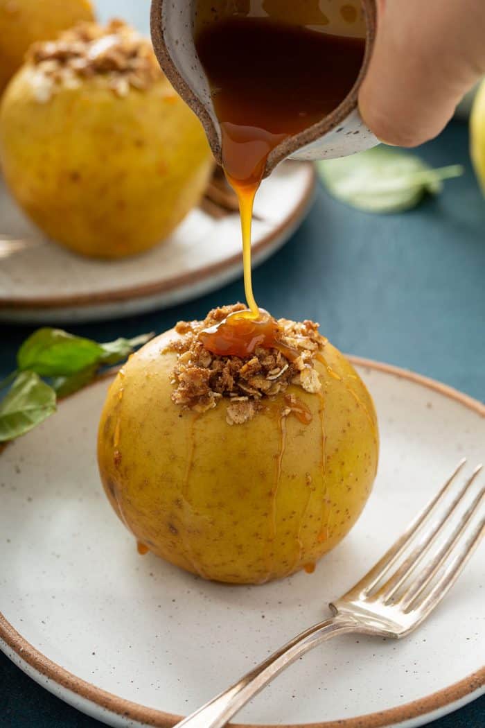 Hand pouring caramel sauce onto a plated baked apple