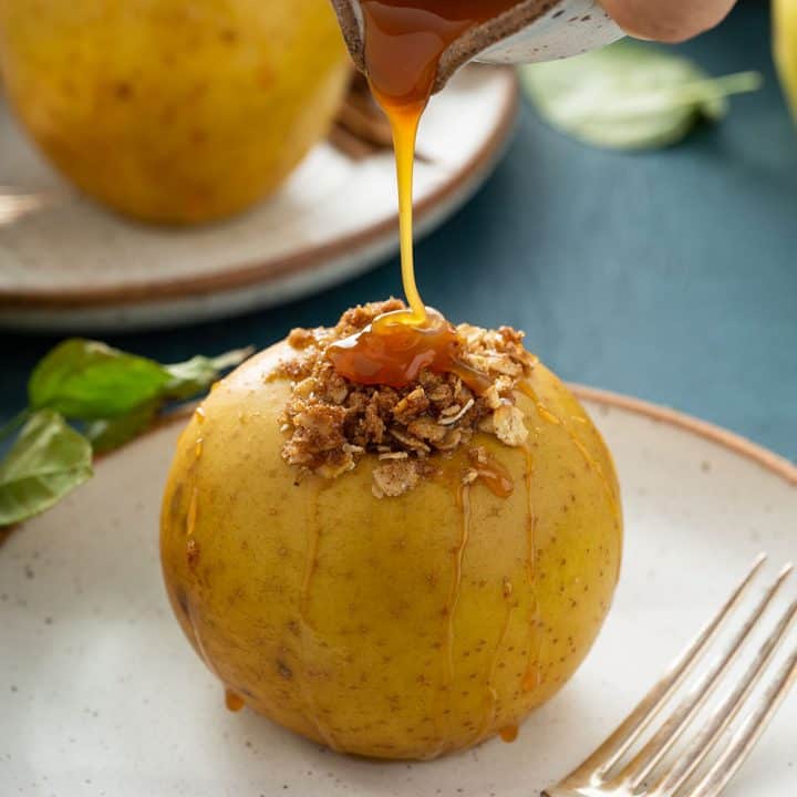 Hand pouring caramel sauce onto a plated baked apple