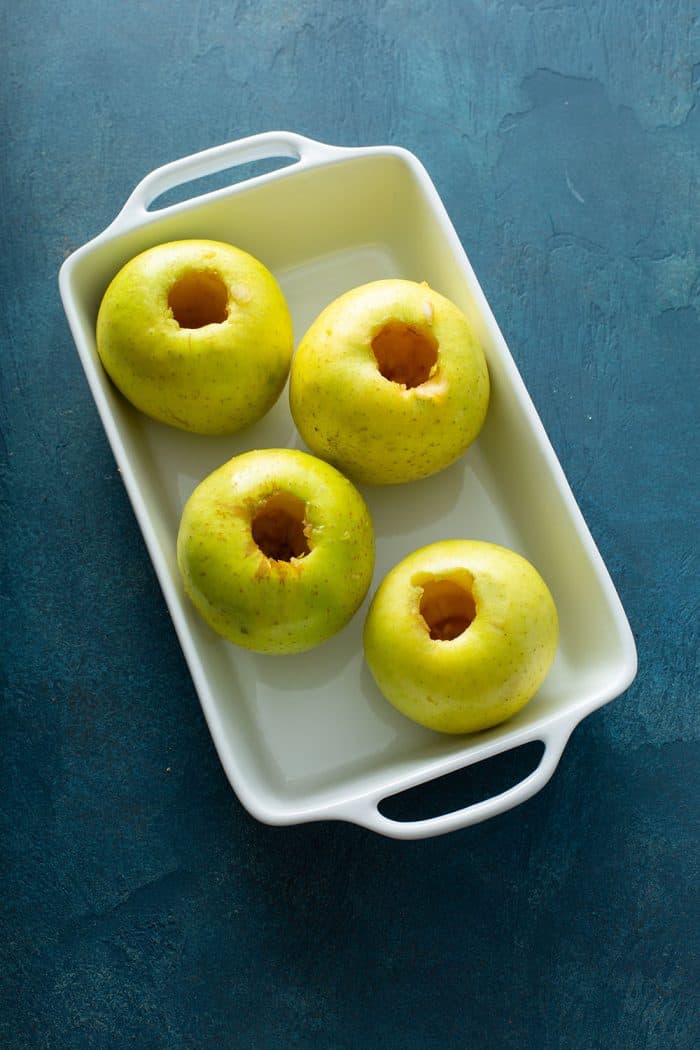 Four cored apples in a white baking dish