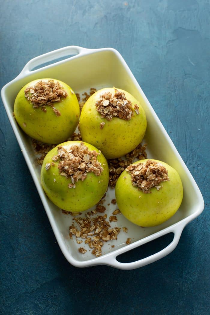 Crumble-stuffed apples in a white baking dish, ready to be baked