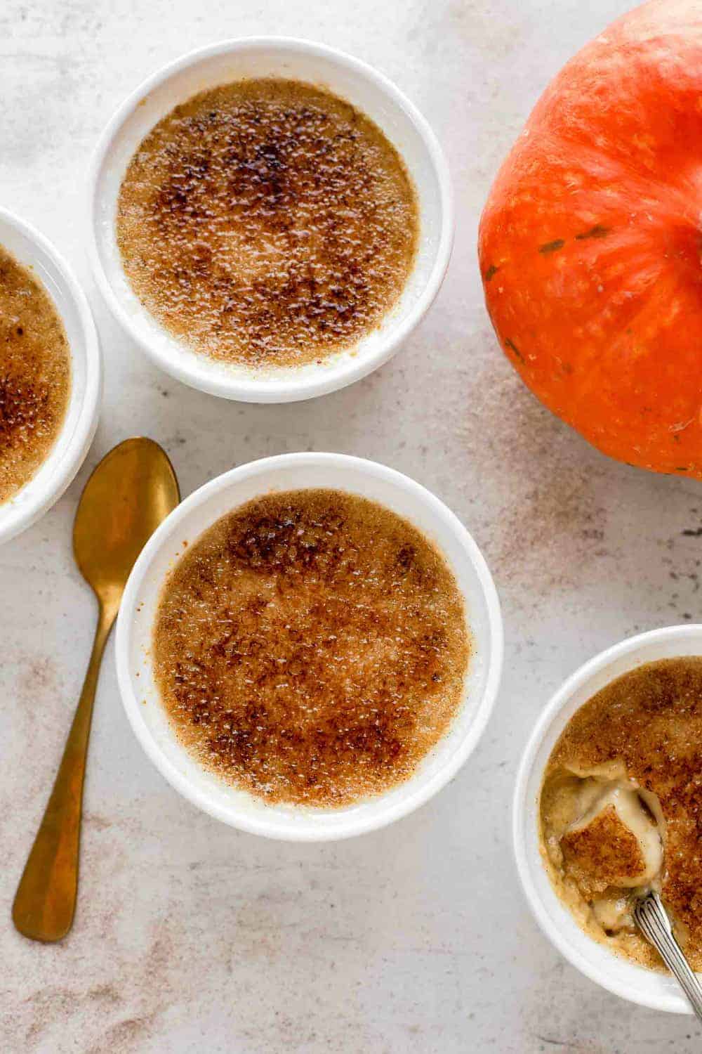 Pumpkin creme brulee in white ramekins, next to a spoon and a pumpkin