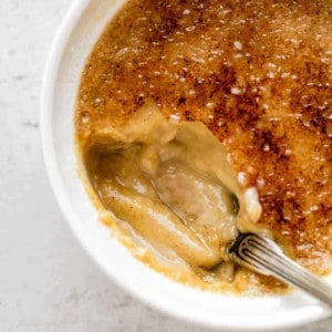 Bite taken out of a pumpkin creme brulee, showing the pumpkin custard underneath the bruleed sugar topping