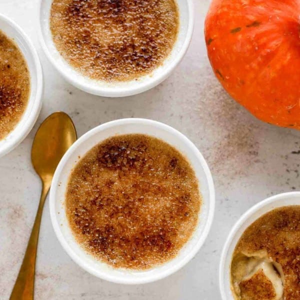 Pumpkin creme brulee in white ramekins, next to a spoon and a pumpkin