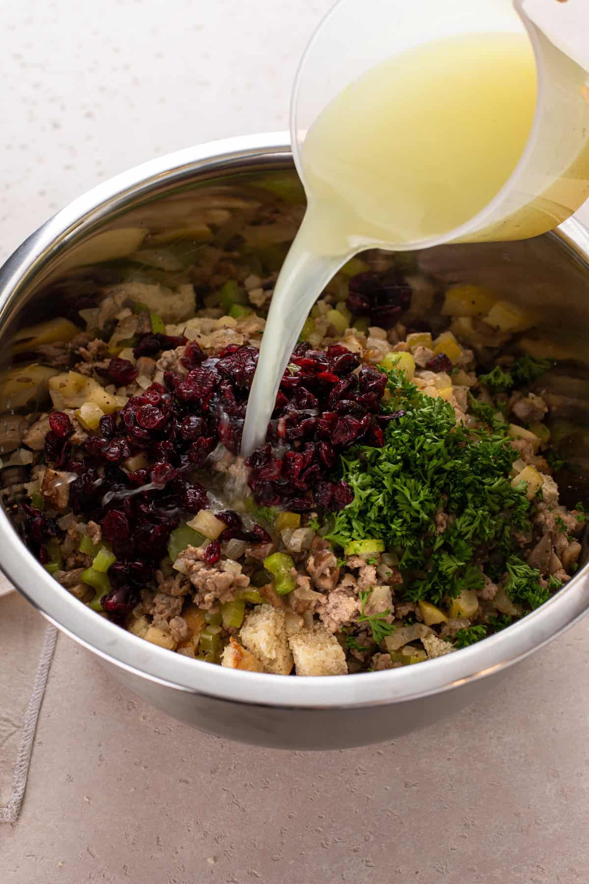 chicken stock being poured over ingredients for sausage and cranberry stuffing in a large bowl.