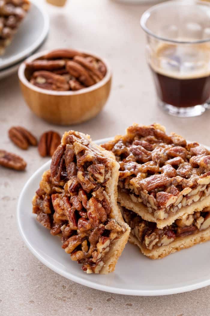One pecan bar with a bite taken from the corner leaning against two stacked pecan bars on a white plate.