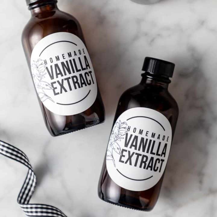 Two small bottles of vanilla extract with printed labels lying on a marble countertop.