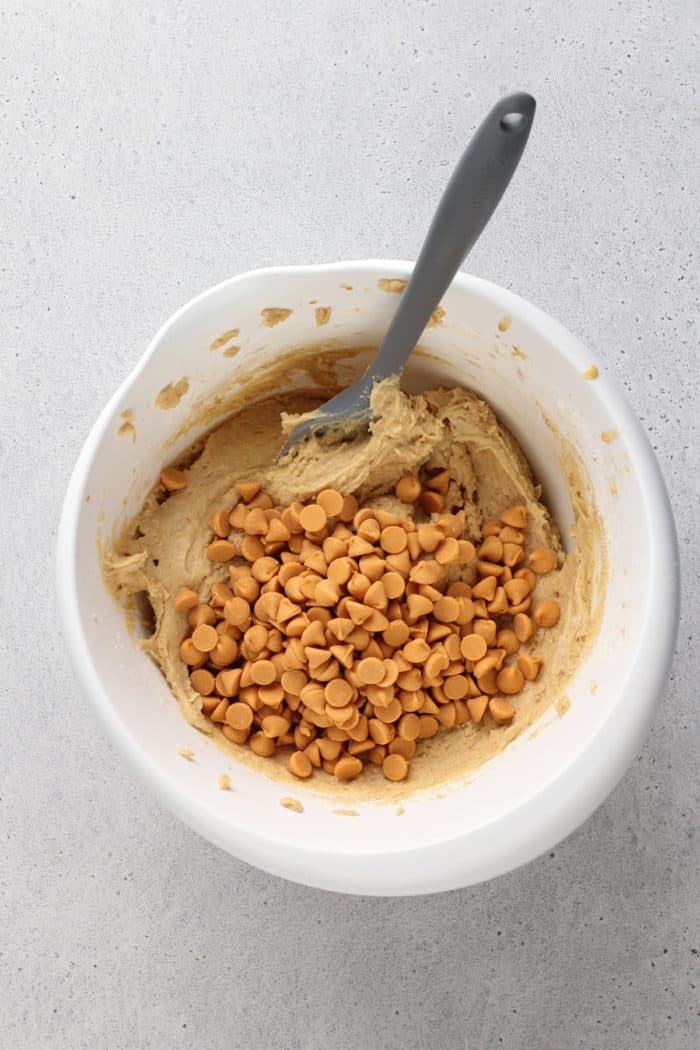 Butterscotch chips being added to brown butter blondie batter in a white mixing bowl.