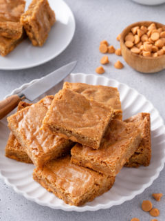 Several brown butter blondies arranged on a white platter, with a knife set on the side of the platter.