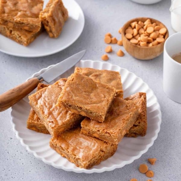 Several brown butter blondies arranged on a white platter, with a knife set on the side of the platter.