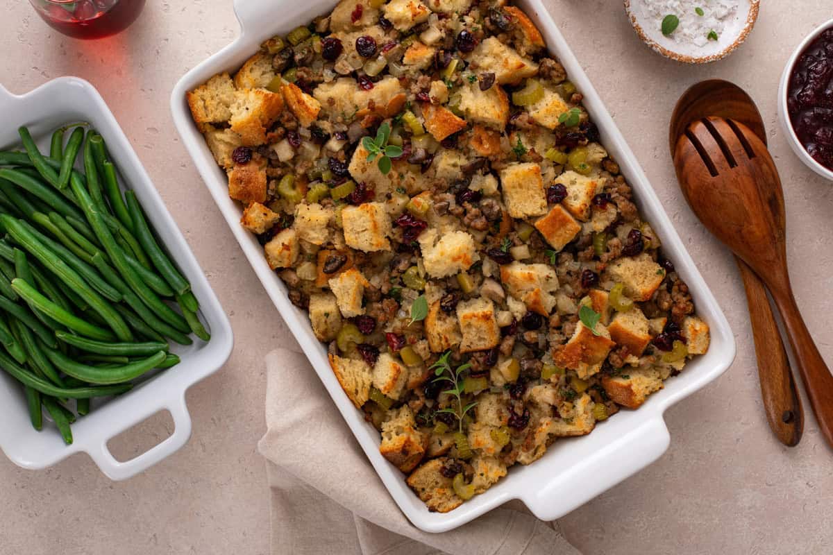 Overhead view of sausage and cranberry stuffing on a countertop next to a bowl of cooked green beans.