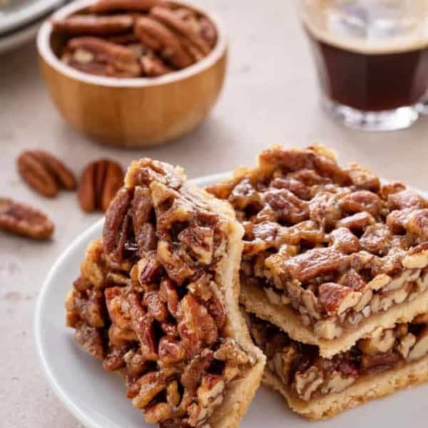 One pecan bar with a bite taken from the corner leaning against two stacked pecan bars on a white plate.