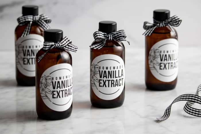 Four small, labeled bottles of homemade vanilla extract on a marble countertop.