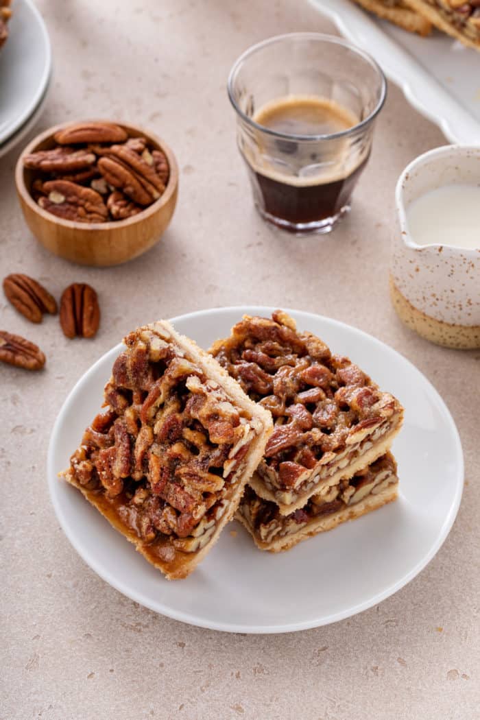 One pecan bar leaning against two stacked pecan bars on a white plate.