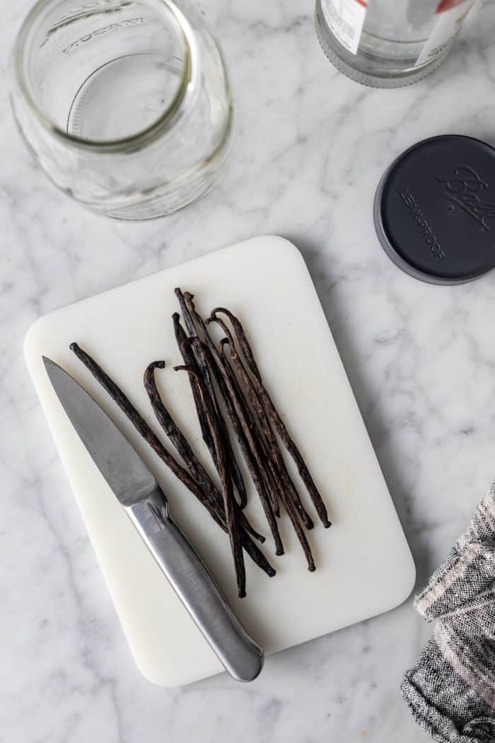 Paring knife on a white cutting board next to vanilla beans.