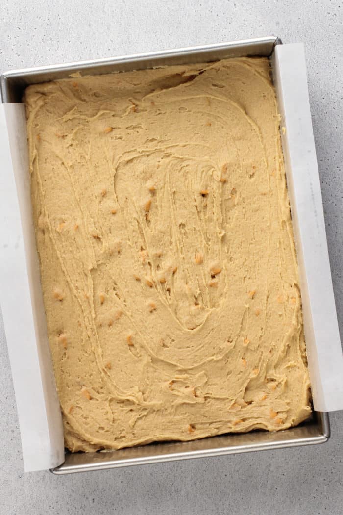 Brown butter blondie batter spread into a parchment-lined baking pan, ready to go in the oven.